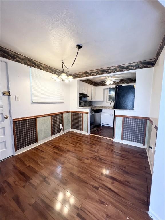 interior space featuring white cabinets, an inviting chandelier, a sink, under cabinet range hood, and dark wood-style floors