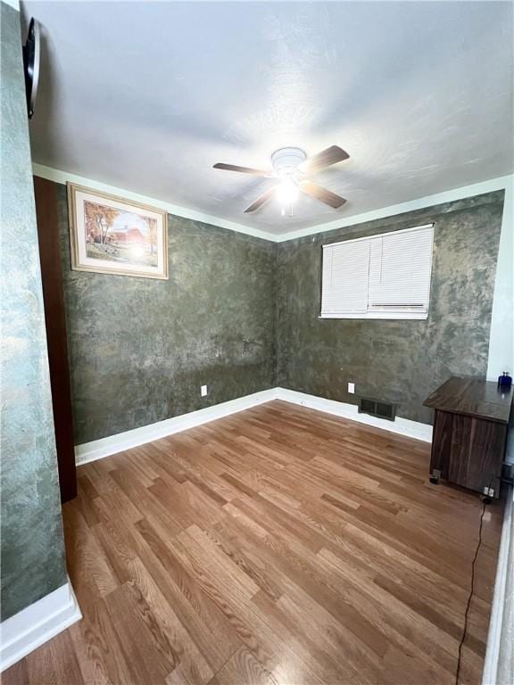 empty room featuring ceiling fan, baseboards, visible vents, and wood finished floors