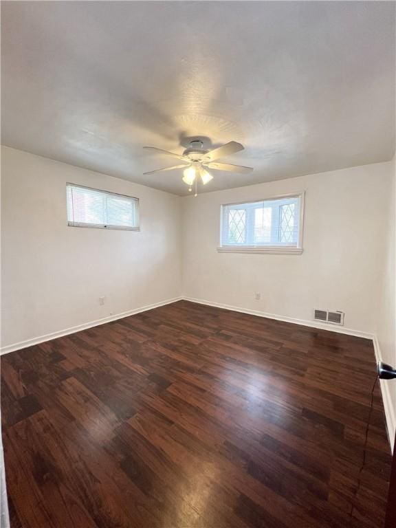 unfurnished room with baseboards, dark wood-style flooring, ceiling fan, and visible vents