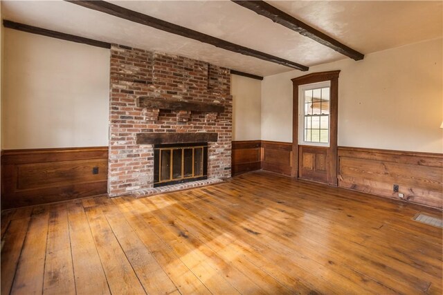 unfurnished living room with beamed ceiling, wooden walls, a brick fireplace, and hardwood / wood-style flooring