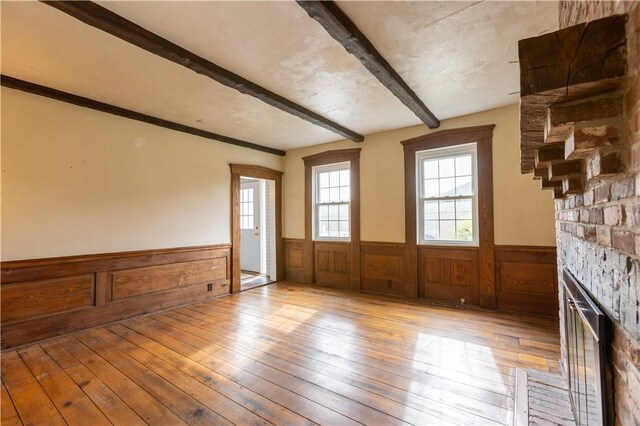 unfurnished room with beamed ceiling, a fireplace, and light hardwood / wood-style flooring