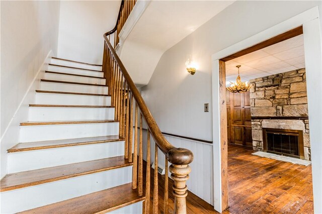 stairway featuring hardwood / wood-style flooring, a stone fireplace, and a notable chandelier