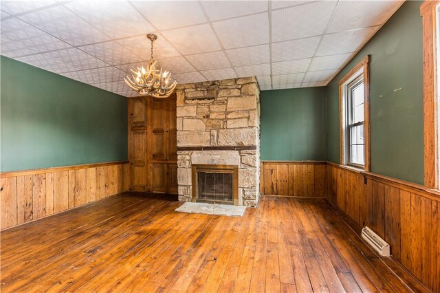 unfurnished living room with wood-type flooring, a chandelier, a fireplace, and wood walls