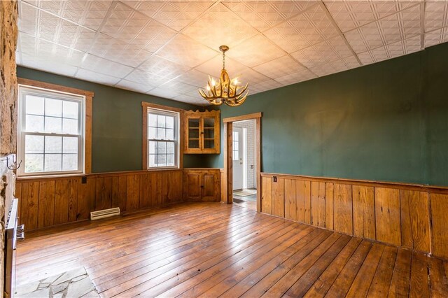 spare room with an inviting chandelier, light hardwood / wood-style flooring, and wood walls