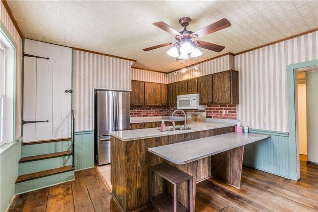 kitchen with wood-type flooring, sink, stainless steel fridge, a kitchen bar, and kitchen peninsula