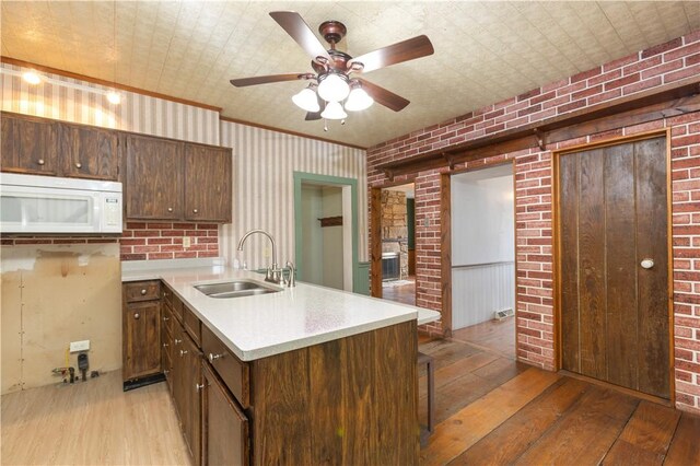 kitchen featuring sink, light wood-type flooring, ornamental molding, ceiling fan, and brick wall