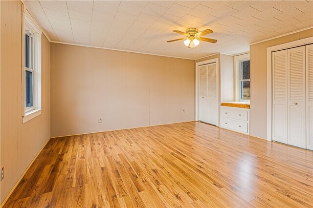 unfurnished bedroom with crown molding, two closets, ceiling fan, and light hardwood / wood-style flooring