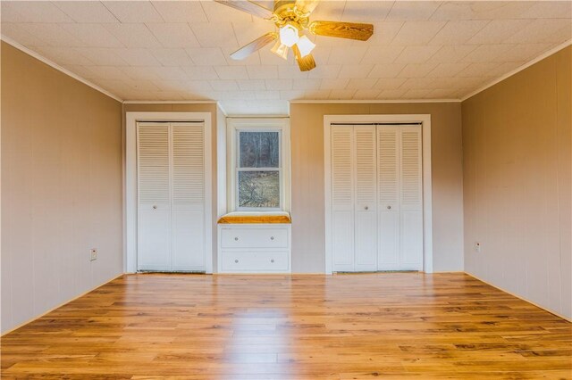 unfurnished bedroom featuring crown molding, ceiling fan, light wood-type flooring, and two closets