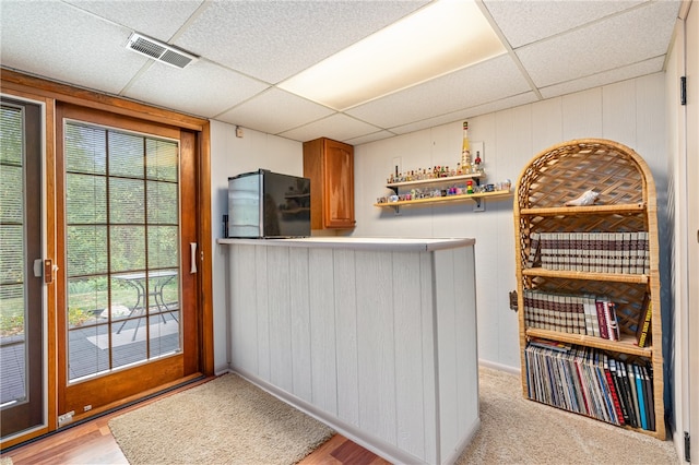 interior space with black fridge, light hardwood / wood-style flooring, a paneled ceiling, and wood walls