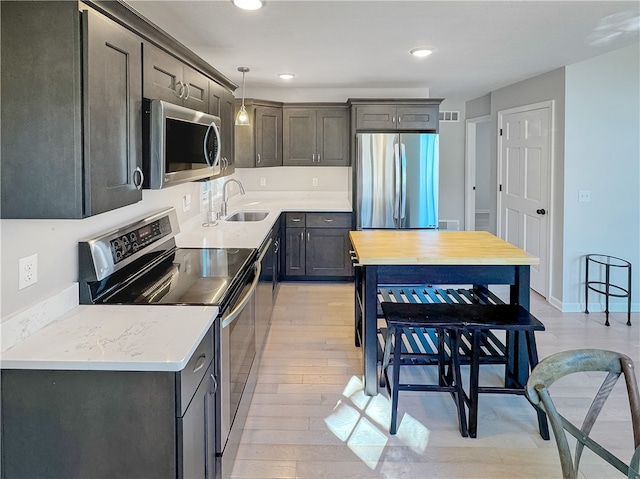 kitchen with decorative light fixtures, appliances with stainless steel finishes, light wood-type flooring, and sink