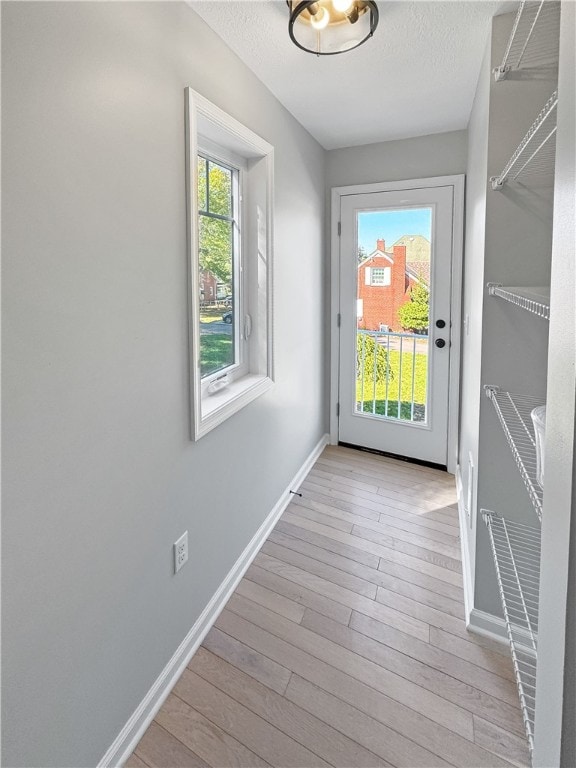 doorway with light hardwood / wood-style floors, a healthy amount of sunlight, and a textured ceiling