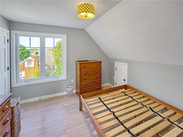 bedroom featuring light wood-type flooring, a textured ceiling, and vaulted ceiling