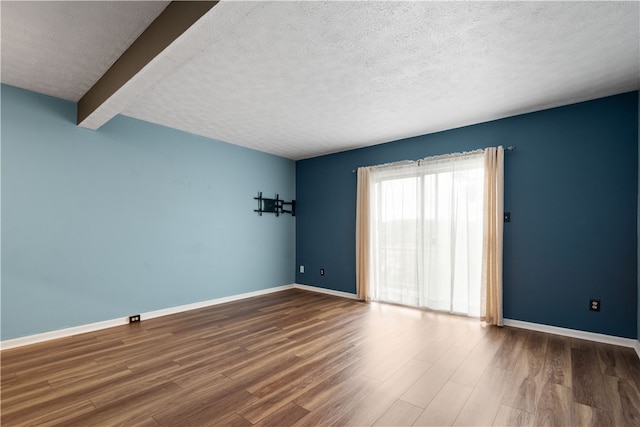 unfurnished room with a textured ceiling, hardwood / wood-style floors, and beamed ceiling