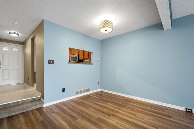 interior space with a textured ceiling, beamed ceiling, and hardwood / wood-style flooring