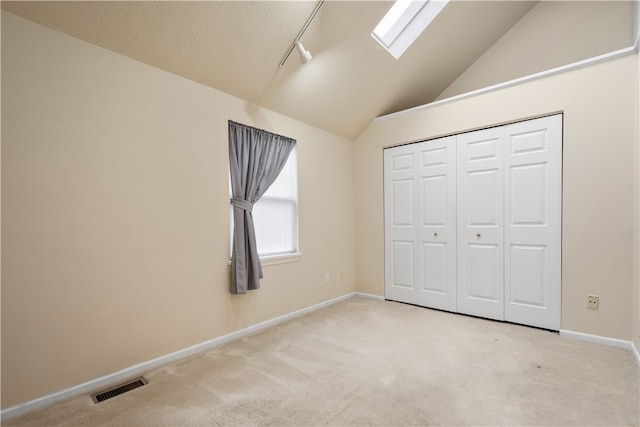 unfurnished bedroom featuring a closet, track lighting, a textured ceiling, light colored carpet, and lofted ceiling with skylight