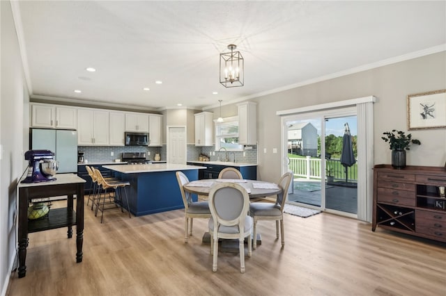 kitchen featuring white cabinets, decorative light fixtures, appliances with stainless steel finishes, a center island, and light hardwood / wood-style floors