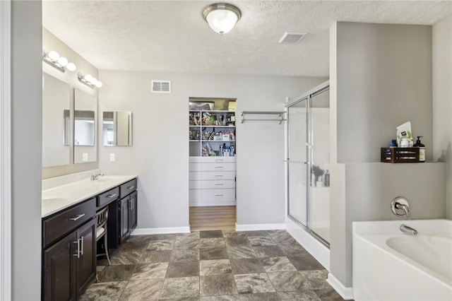 bathroom with a textured ceiling, vanity, and separate shower and tub