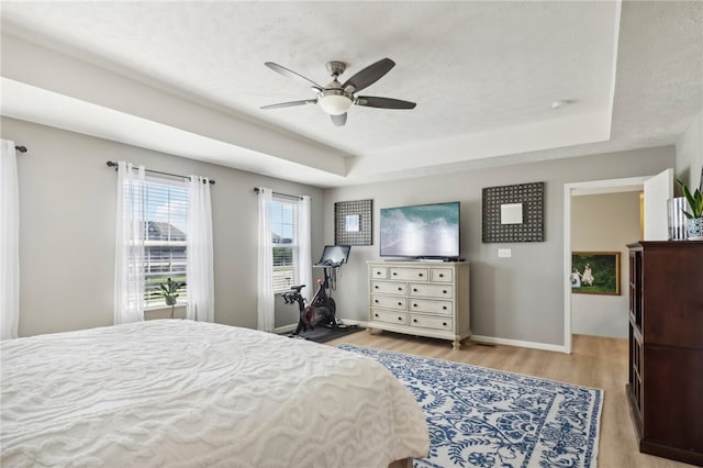 bedroom with ceiling fan, a textured ceiling, light hardwood / wood-style flooring, and a tray ceiling