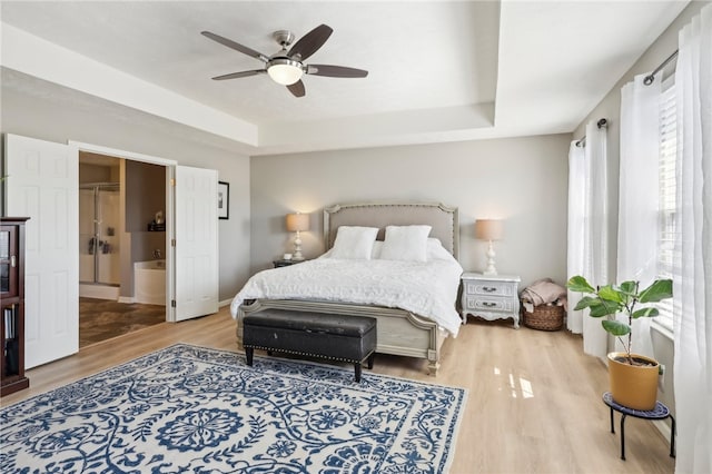 bedroom featuring wood-type flooring, connected bathroom, a tray ceiling, and ceiling fan