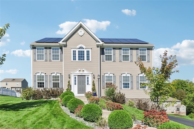 colonial house featuring a front yard and solar panels