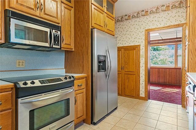 kitchen with light tile patterned floors, stainless steel appliances, and wooden walls