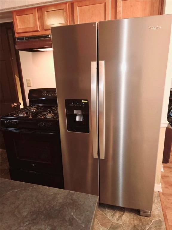 room details featuring gas stove, stainless steel refrigerator with ice dispenser, exhaust hood, light tile patterned floors, and dark stone countertops