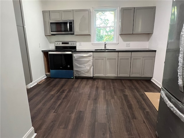 kitchen with appliances with stainless steel finishes, sink, dark wood-type flooring, and gray cabinets