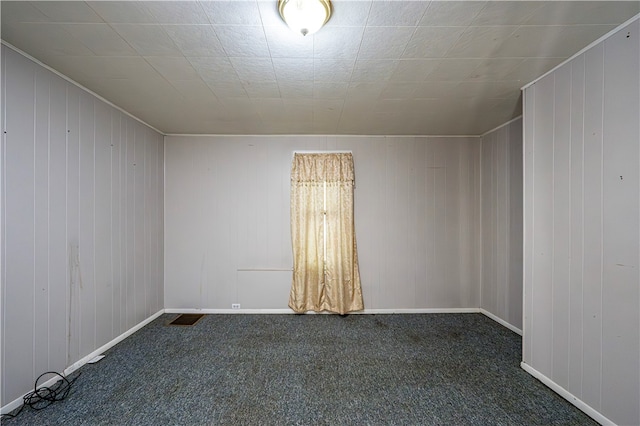 carpeted empty room featuring wooden walls