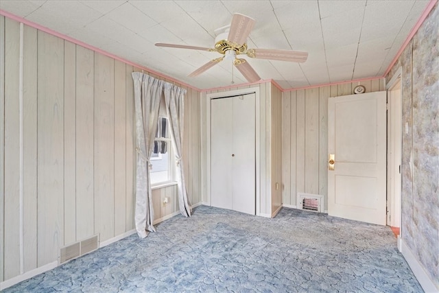 carpeted empty room with wood walls and ceiling fan