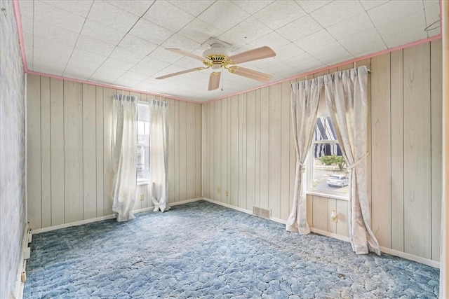 carpeted spare room featuring wooden walls and ceiling fan