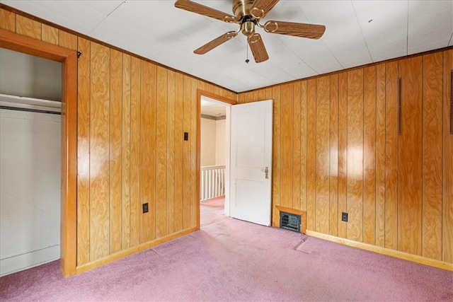 unfurnished bedroom featuring ceiling fan, light colored carpet, and wood walls