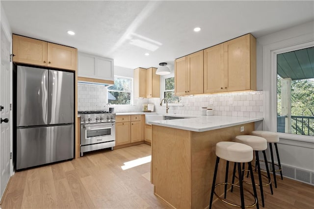 kitchen with a breakfast bar, light brown cabinets, light wood-type flooring, appliances with stainless steel finishes, and kitchen peninsula