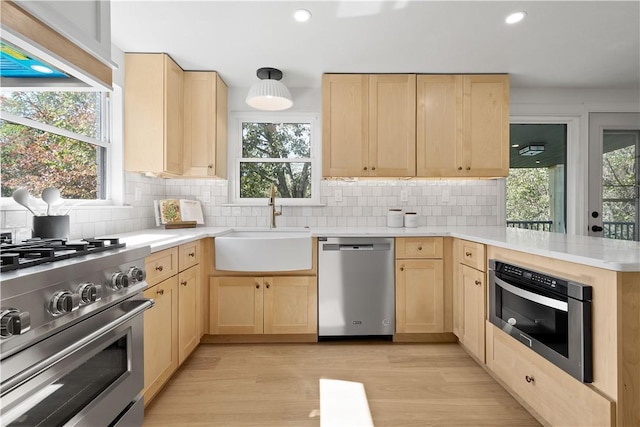 kitchen with sink, light wood-type flooring, kitchen peninsula, stainless steel appliances, and extractor fan