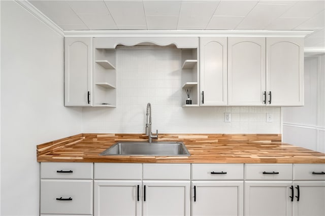 kitchen with white cabinetry, tasteful backsplash, butcher block counters, ornamental molding, and sink