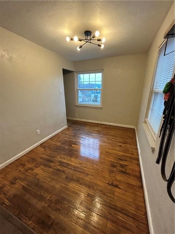 empty room with dark hardwood / wood-style flooring, a chandelier, and a textured ceiling