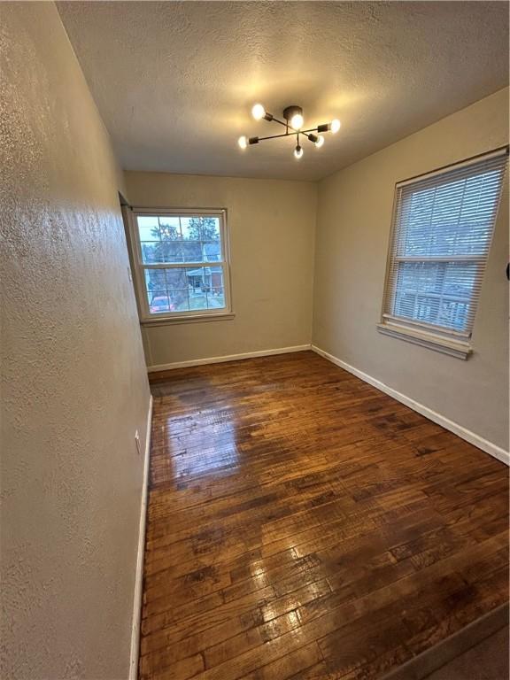 spare room with dark wood-type flooring, a textured ceiling, and a notable chandelier