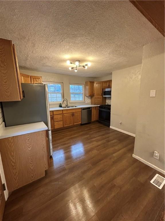 kitchen with a textured ceiling, stainless steel appliances, dark wood-type flooring, and sink