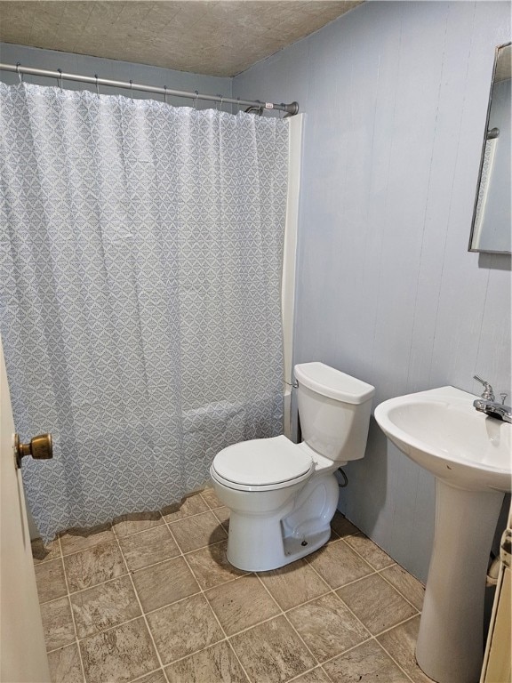 bathroom with a textured ceiling, wooden walls, curtained shower, and toilet