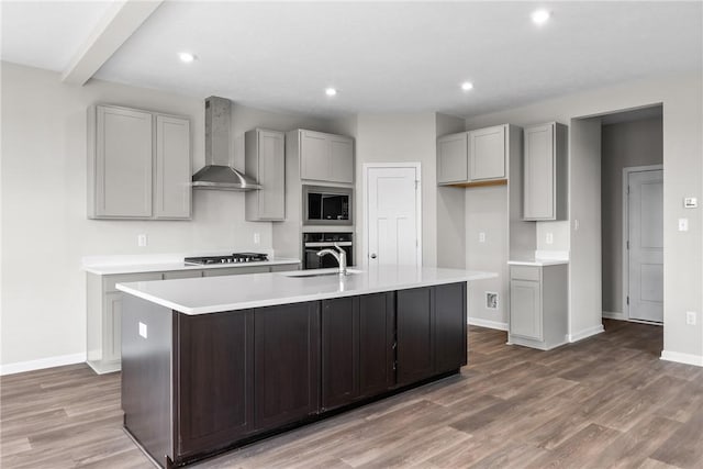 kitchen featuring appliances with stainless steel finishes, dark wood-type flooring, wall chimney range hood, gray cabinets, and an island with sink