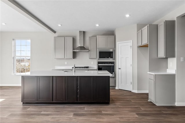 kitchen featuring an island with sink, stainless steel appliances, gray cabinetry, and wall chimney range hood