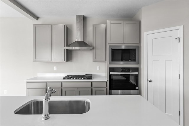 kitchen with gray cabinetry, sink, wall chimney exhaust hood, a textured ceiling, and appliances with stainless steel finishes