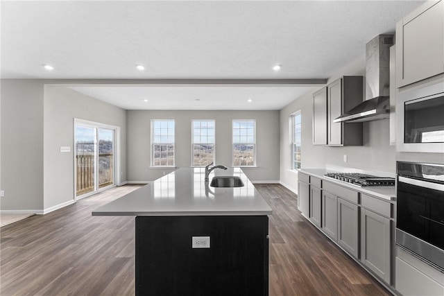 kitchen featuring sink, wall chimney range hood, dark hardwood / wood-style floors, an island with sink, and stainless steel gas stovetop