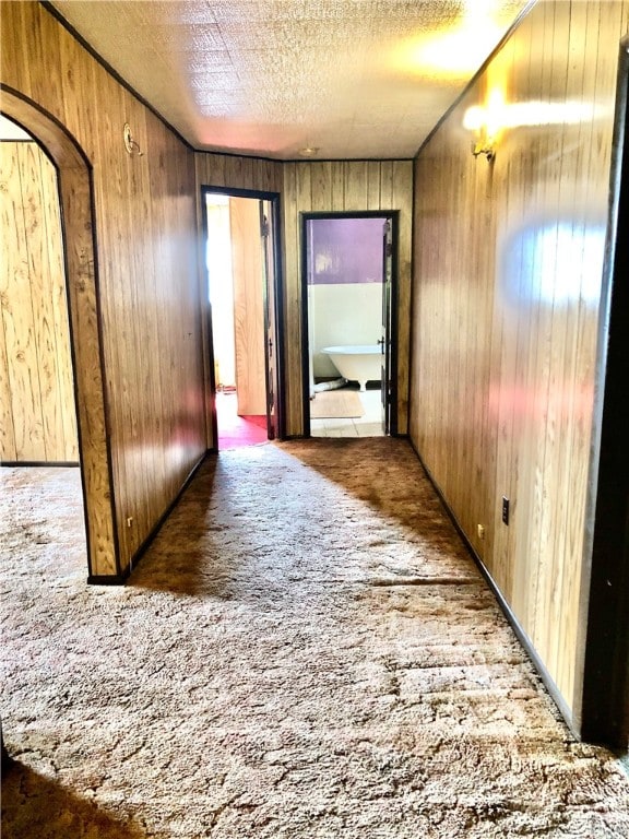 hallway featuring wooden walls, dark colored carpet, and a textured ceiling