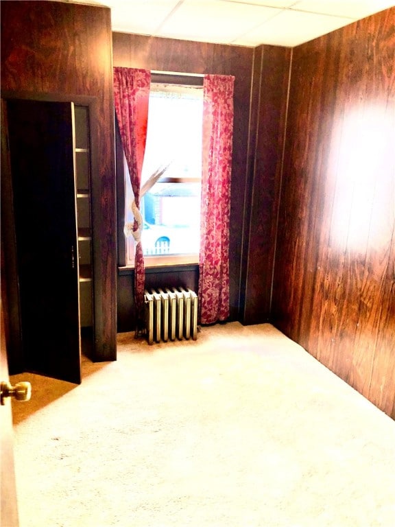 spare room with carpet, wooden walls, and radiator heating unit