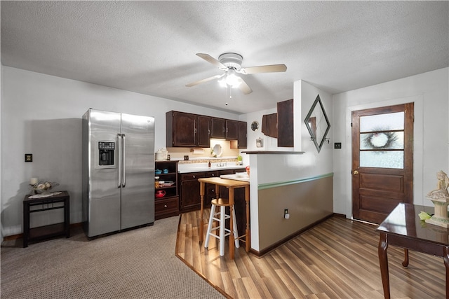 kitchen featuring a textured ceiling, light wood-type flooring, dark brown cabinets, ceiling fan, and stainless steel refrigerator with ice dispenser