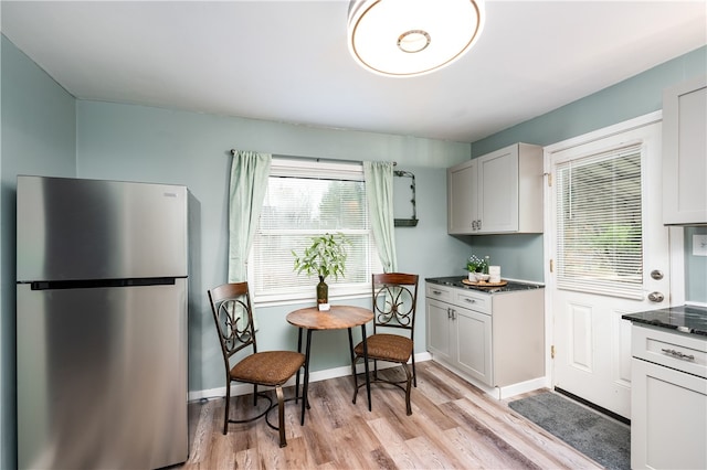 kitchen featuring white cabinets, dark stone countertops, stainless steel refrigerator, and light hardwood / wood-style flooring