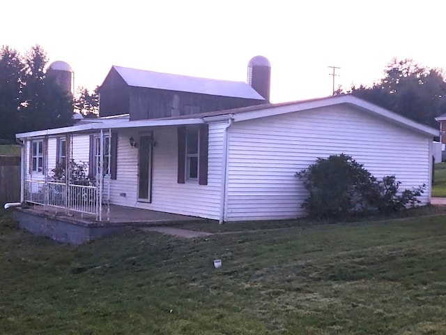 property exterior at dusk with covered porch and a lawn