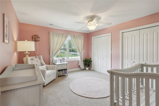 carpeted bedroom with ceiling fan, a nursery area, and two closets