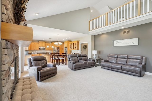 carpeted living room with a notable chandelier, a stone fireplace, and high vaulted ceiling