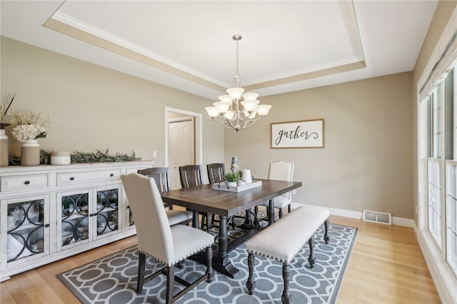 dining room with light wood-type flooring, a tray ceiling, and a wealth of natural light